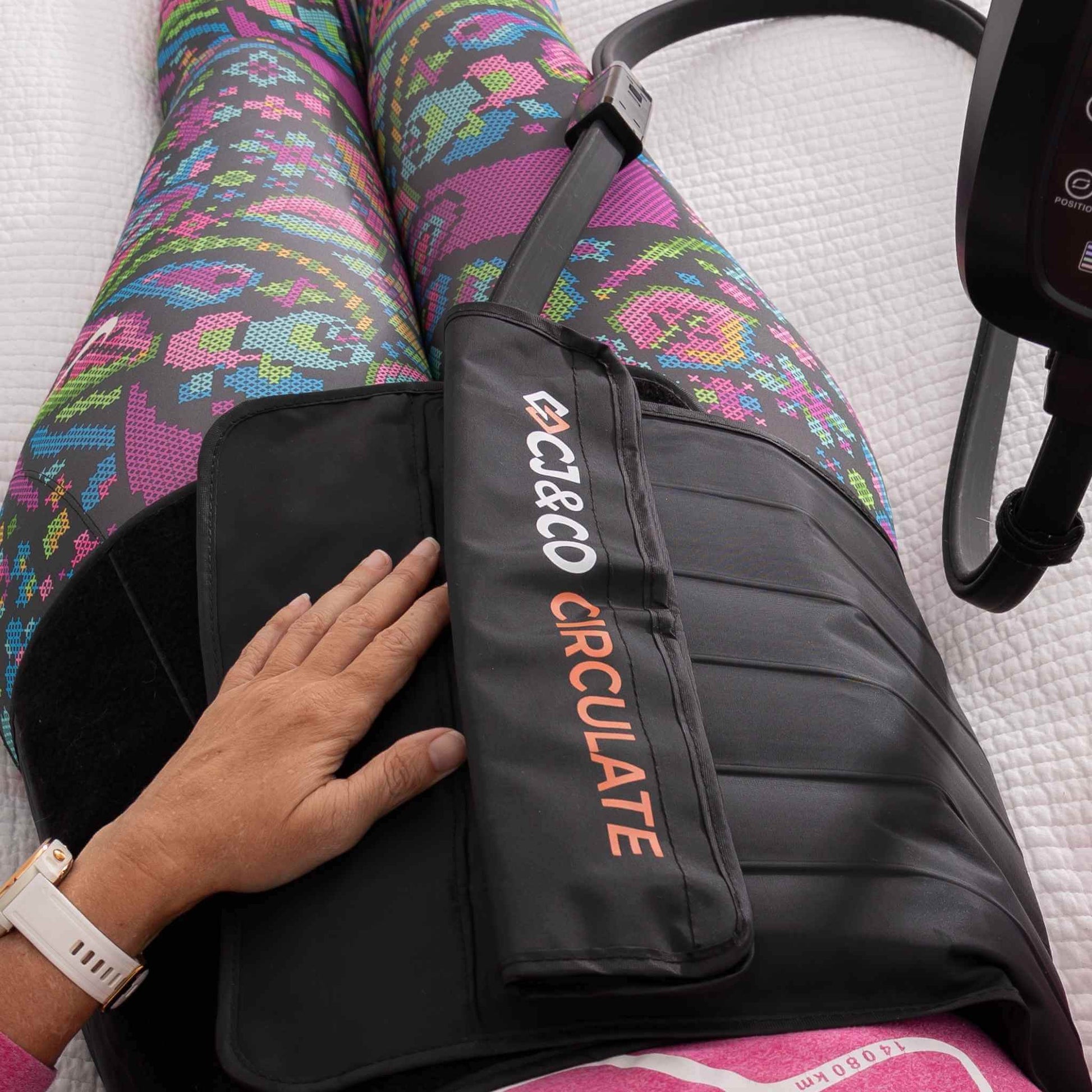 Person wearing colorful leggings with a black Circulate compression garment on a white surface
