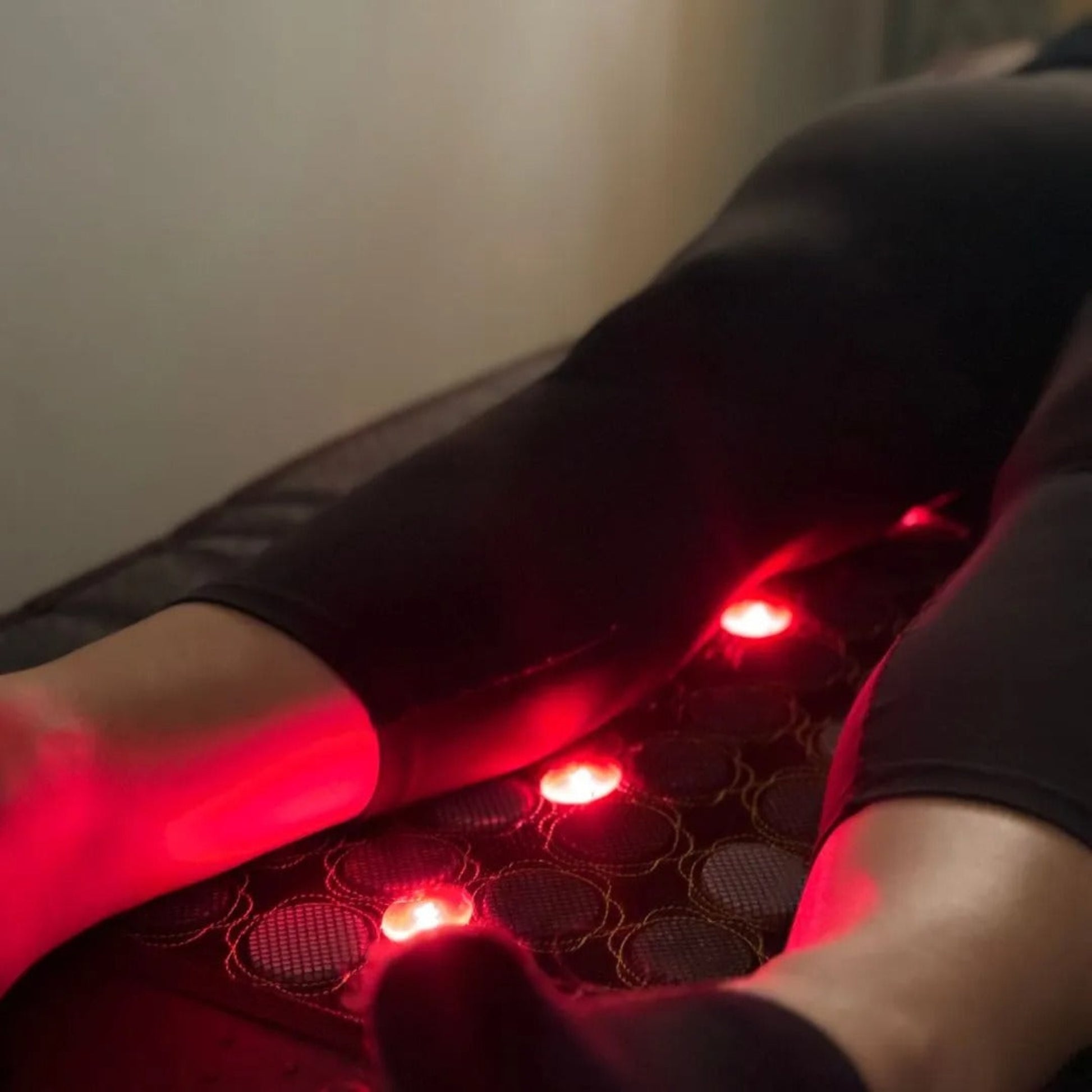Person using a massage mat with red lights on a plain background