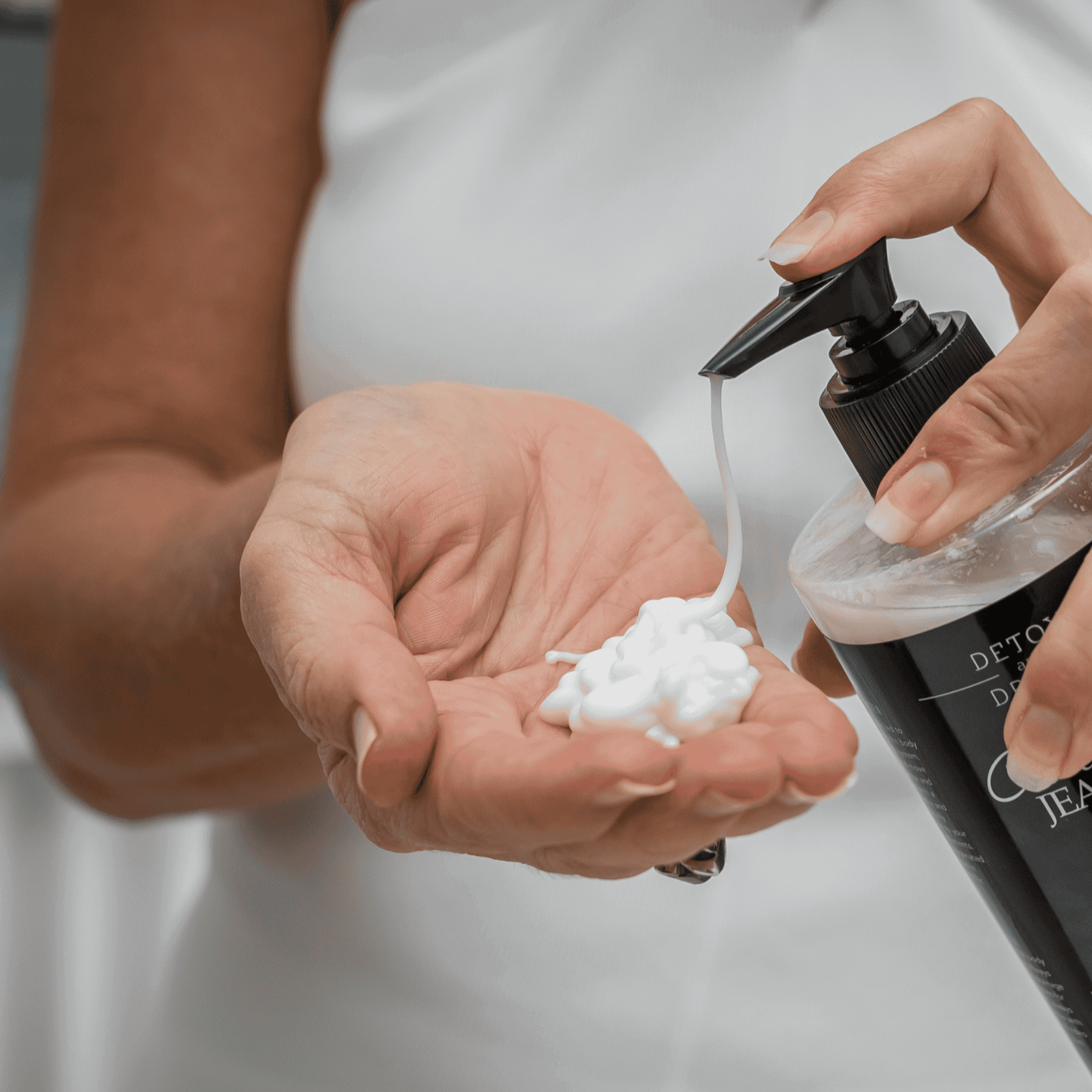 Person holding a bottle of skincare product with cream in their palm
